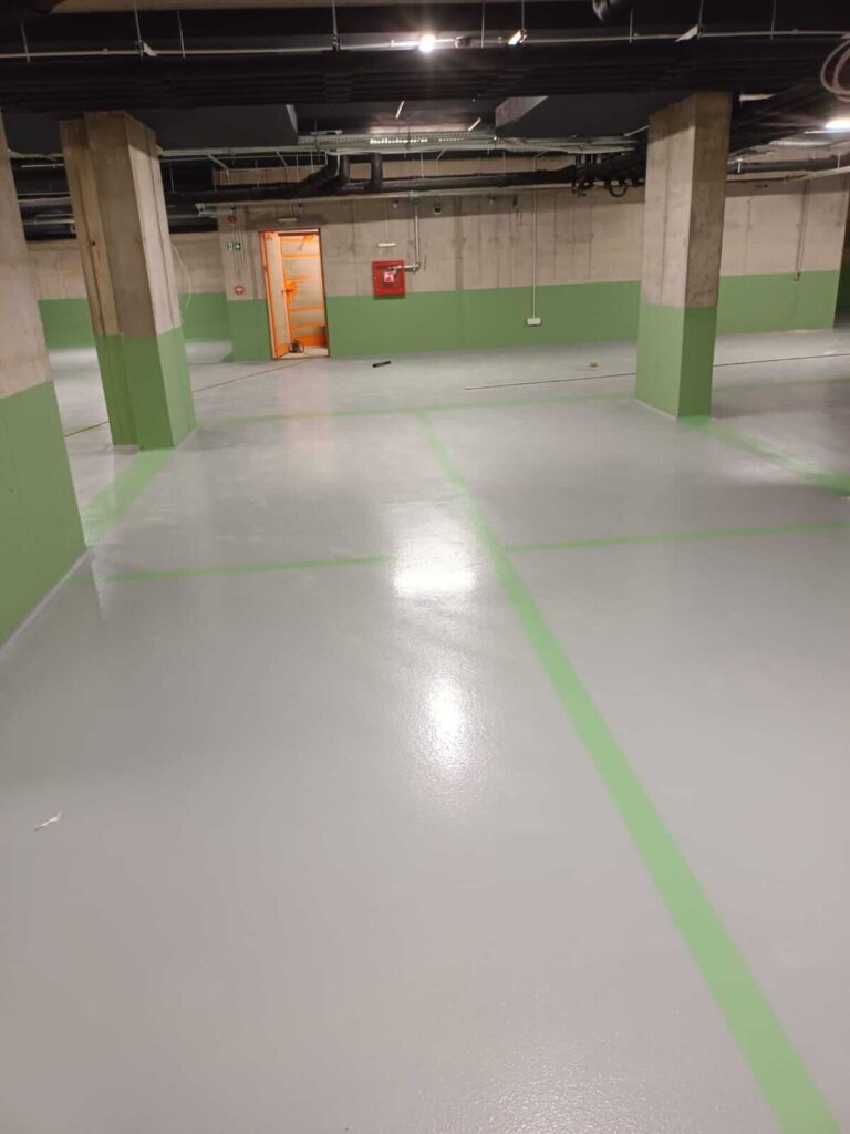 Pardoseală epoxidică industrială gri pentru parcare subterană, cu marcaje verzi și finisaj rezistent